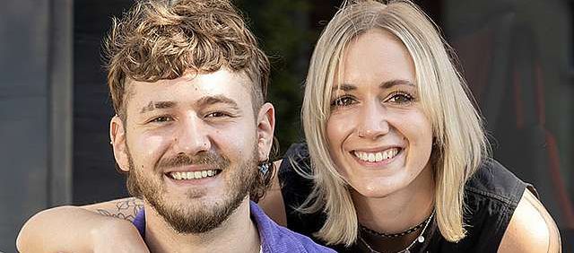 Eine Frau legt vor einer KVV-Bahn ihren Arm um die Schulter eines Mannes.